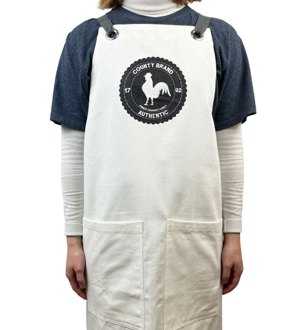 natural colour apron with grey straps and rooster badge county brand design in black